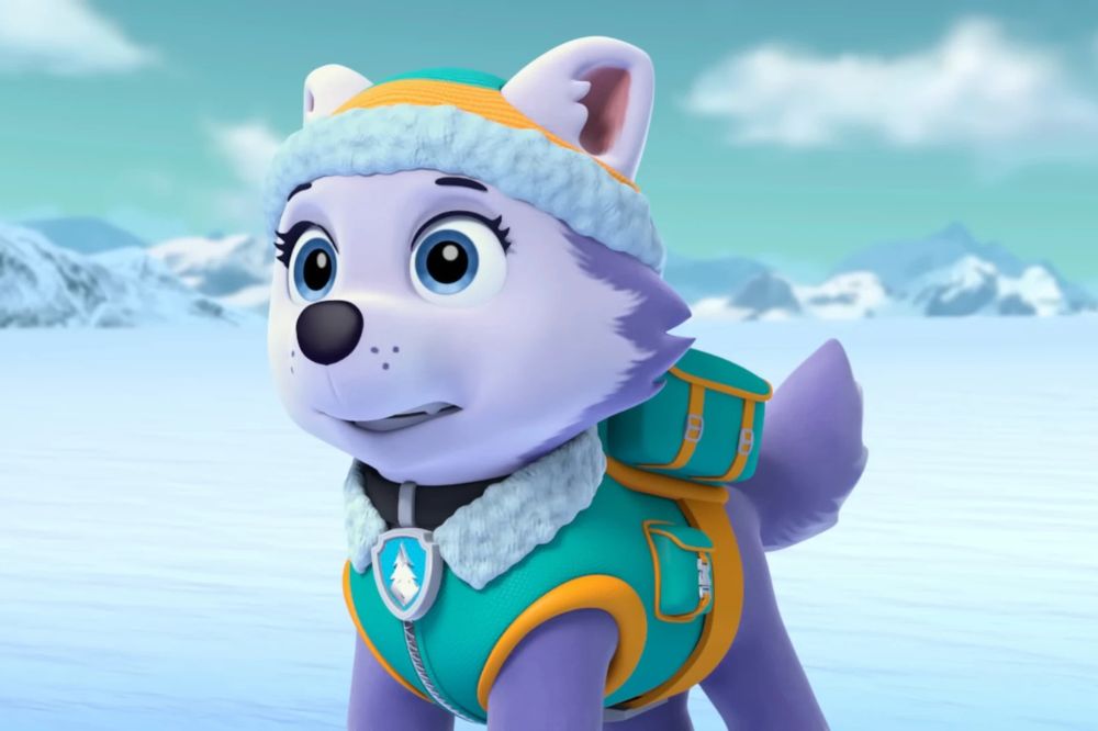 Everest, la chienne husky de la Pat’ Patrouille, portant une tenue d’hiver turquoise et orange dans un paysage enneigé.